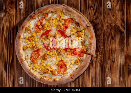 Pizza für Kinder auf Sahnebasis mit Hühnerfilet, Tomaten, Mais und Mozzarella-Käse auf Holzhintergrund. Stockfoto