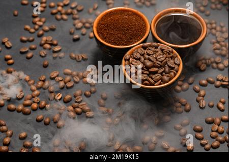 Tassen Kaffee unter ausgewählten und kalibrierten Arabica-Kaffeebohnen, verteilt auf schwarzem Hintergrund, drei aromatische Tassen Kaffee in einem Paar. Stockfoto