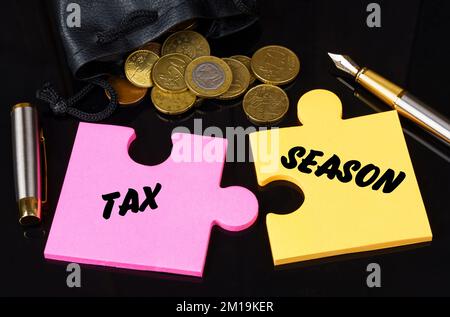 Geschäfts- und Finanzkonzept. Münzen sind auf der schwarzen Oberfläche verstreut, es gibt einen Stift und Rätsel, auf denen sie geschrieben sind - STEUERSAISON Stockfoto