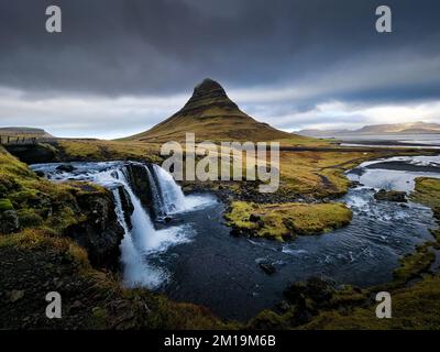 Wasserfall mit bewölktem Himmel und grünem Gras in Island. Kirkjufell Stockfoto