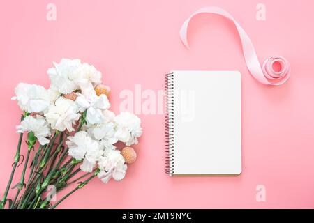 Leerer Notizblock und Blumenstrauß auf pinkfarbenem Hintergrund, flach liegend. Stockfoto