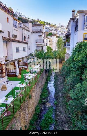 Malerisches Dorf mit weißen Häusern mit kleinem Bach, der sich neben den Häusern rund um das Dorf Setenil de las Bodegas, Cadiz, windet. Stockfoto