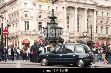 Piccadilly Circus an einem geschäftigen Tag, Piccadilly, London, Großbritannien; viele Menschen stehen und gehen über den zentralen Abschnitt des Circus; Gebäude um t Stockfoto