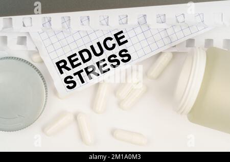 Medizin und Gesundheitskonzept. Auf dem Tisch ist ein offenes Glas mit Pillen und ein Blatt Papier mit der Aufschrift - reduzieren Sie Stress Stockfoto