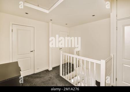 Ein leerer Raum mit weißen Wänden und schwarzem Teppichboden, es gibt eine Treppe, die in die zweite Etage führt Stockfoto