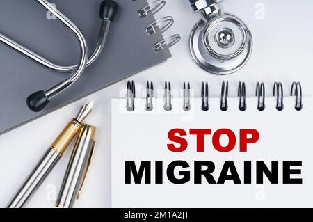 Medizin und Gesundheitskonzept. Auf dem Tisch befinden sich ein Stethoskop, ein Stift und ein Notizbuch mit der Aufschrift - STOPP MIGRÄNE Stockfoto