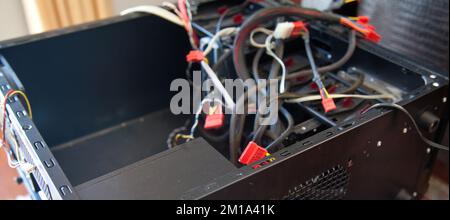 Desktop-Computer, schwarzes leeres Gehäuse und verschiedene Kabel, die versucht werden, in einer häuslichen Umgebung montiert zu werden Stockfoto