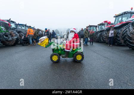 Bridgnorth, Shropshire, Vereinigtes Königreich. 11.. Dezember 2022. Ein kleiner Junge, der als Weihnachtsmann verkleidet ist, fährt mit seinem Spielzeugtraktor zu den echten Traktoren, die sich für den Bridgnorth Festive Charity Tractor Run 2022 versammelten. Über 100 landwirtschaftliche Traktoren bildeten eine Prozession und fuhren vom Bridgnorth Viehmarkt durch die Dörfer von Shropshire, um Geld für Hope House Children's Hospices zu sammeln. Kredit: Peter Lopeman/Alamy Live News Stockfoto