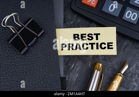 Finanz- und Geschäftskonzept. Auf der Tabelle befinden sich ein Taschenrechner, ein Stift und ein Notizbuch mit einem Lesezeichen, auf dem es geschrieben ist – BEST PRACTICE Stockfoto