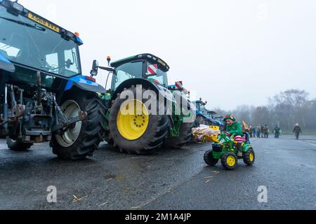 Bridgnorth, Shropshire, Vereinigtes Königreich. 11.. Dezember 2022. Ein kleiner Junge fährt mit seinem Spielzeugtraktor zu den echten Traktoren, die sich für den Bridgnorth Festive Charity Tractor Run 2022 versammelten. Über 100 landwirtschaftliche Traktoren bildeten eine Prozession und fuhren vom Bridgnorth Viehmarkt durch die Dörfer von Shropshire, um Geld für Hope House Children's Hospices zu sammeln. Kredit: Peter Lopeman/Alamy Live News Stockfoto