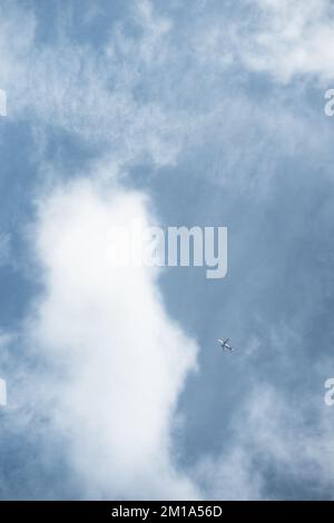 Ein Fernflugzeug fliegt gegen einen blauen Himmel mit nebligen weißen Wolken. Stockfoto