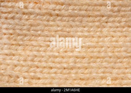 Das gestrickte Nahmuster liegt flach in natürlichem Beige. Makro gestricktes Muster oben in goldener Farbe. Pullover-Muster Stockfoto