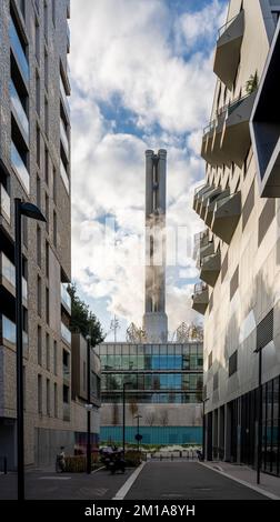 Blick auf eine enge Straße zwischen zwei Gebäuden und einen rauchenden Industriekamin im Hintergrund Stockfoto