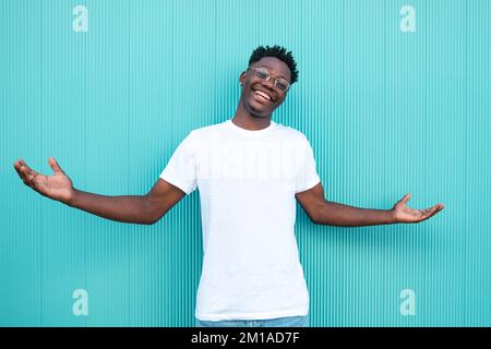 Porträt eines glücklichen afroamerikanischen Kerls, der mit weit geöffneten Armen lächelt, mit türkisfarbenem Hintergrund und weißem T-Shirt. Stockfoto