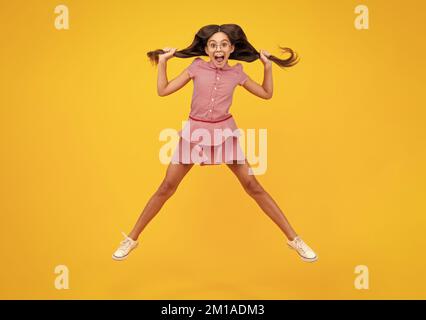 Ein erstaunlicher Teenager. In voller Länge überglücklich Teenager Kind Mädchen 12 13 14 Jahr in Freizeitkleidung springen alt isoliert auf gelbem Hintergrund Studio. Witziger Sprung Stockfoto