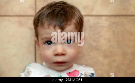 Porträt eines traurigen kleinen Jungen, der auf den gelben Bodenfliesen liegt Stockfoto