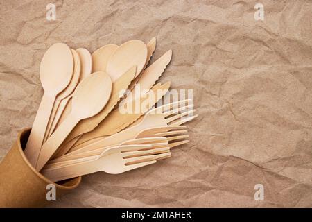 Holzgabeln, Löffel und Messer in Pappbechern auf zerknittertem Papier Stockfoto