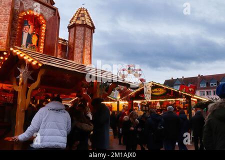 Hanau, Deutschland - 15. Dezember 2019: Menschen und Gebäude auf einem Weihnachtsmarkt mit einer Fahrt im Hintergrund an einem bewölkten Tag in Hanau, Deutschland. Stockfoto