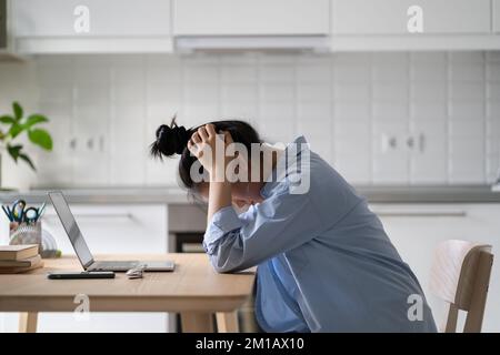 Gestresste, frustrierte Freiberuflerin, die zu Hause vor einem Notebook sitzt und sich unmotiviert fühlt Stockfoto