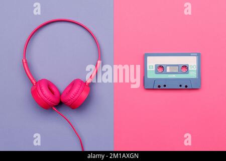 B-Seite der blauen Audiokassette auf pinkfarbenem Hintergrund und pinkfarbene Kopfhörer auf violettem Hintergrund. Analoges Audio-Musikkonzept Stockfoto