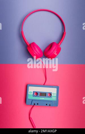 B-Seite der blauen Audiokassette auf pinkfarbenem Hintergrund und pinkfarbene Kopfhörer auf violettem Hintergrund. Analoges Audio-Musikkonzept Stockfoto