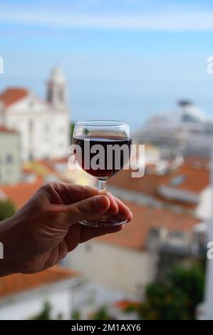 Hand mit einem Glas des portugiesischen Weins porto im Café im Freien am Aussichtspunkt in der farbenfrohen Altstadt von Lissabon, Portugal Stockfoto