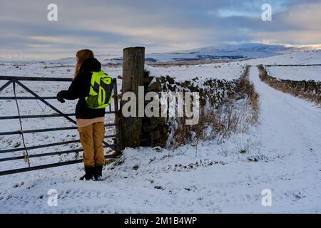 Ein Mädchen im Teenageralter bewundert die Aussicht auf einem Winterspaziergang im Schnee in der Landschaft der Yorkshire Dales mit Ingleborough Hill im Hintergrund Stockfoto