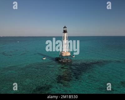 Luftaufnahme eines Leuchtturms umgeben von ruhigem türkisfarbenem und blauem Meer mit einigen Fischerbooten in der Nähe Stockfoto