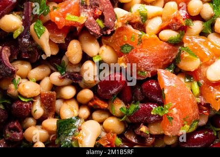 Konsistenz des veganen Salats mit Bohnen-Tomaten und Koriander als Hintergrund. Ein naher Salat mit Bohnen, Tomaten und Koriander. Makrofoto. Homemad Stockfoto