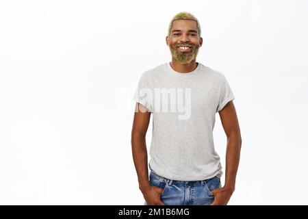 Lächelnder Hipster mit gelbem Bart und Haar, glücklich und selbstbewusst, trägt graues Hemd, Studiohintergrund Stockfoto