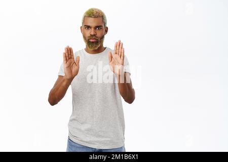 Der Mann sieht besorgt aus, zeigt Stopp, unterbindet Gesten, pausiert, steht über weißem Hintergrund Stockfoto