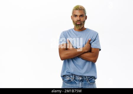 Junge Profis. Ein hübscher, lächelnder Hipster mit gelber Frisur und Bart, Armkreuzungen auf der Brust, selbstbewusst und glücklich aussehend, weißer Hintergrund Stockfoto