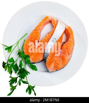 Rohe Lachssteaks, Petersilie, Knoblauch und Zitrone auf dem Teller Stockfoto