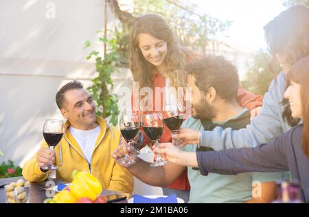 Fröhliche Freunde, die Spaß im Freien haben - eine Gruppe von Freunden, die zu Hause bei Sonnenuntergang auf Weinglas toasten Stockfoto