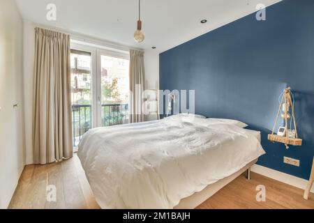 Ein Schlafzimmer mit blauen Wänden und weißer Bettwäsche in der Mitte des Zimmers, es gibt einen Holzfußboden Stockfoto