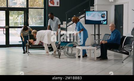 Vater trägt bewusstloses Kind im Gesundheitszentrum, um Hilfe von Fachärzten zu erhalten, besorgte Eltern warten auf Notfallkonsultation mit dem Arzt. Ein medizinisches, krankes Mädchen in der Lobby. Stockfoto