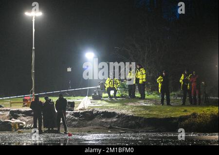 Babbs Mill Park, Solihull, 11. Dezember 2022. Taucher von der Nottinghamshire Police sind angekommen und suchen den Babbs Mill Lake nach 2 Personen, die immer noch vermisst werden, nachdem 4 andere gerettet wurden, nachdem sie am Sonntagabend durch das dünne Eis gefallen waren. Der Taucher tauchte regelmäßig mit grünem Unkraut bedeckt auf, was die schwierigen Arbeitsbedingungen veranschaulicht. Die West Midlands Police hatte früher eine Unterwasserdrohne benutzt, um die Vermissten zu lokalisieren. Feuerwehr und Krankenwagen mit spezialisierten Wasserrettungsteams sind immer noch am Einsatzort in der Nähe der Fordbridge Road, Kingshurst, Solihull England. Quelle: Stop Press Media/Alamy L Stockfoto