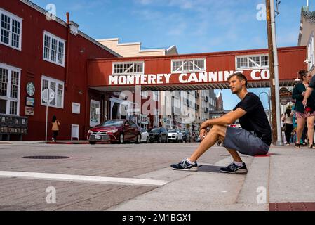 Rücksichtsvoller Mann, der auf dem Bürgersteig sitzt, mit der Monterey Canning Company im Hintergrund Stockfoto