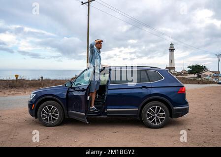 Ein Mann, der im Auto steht und wegschaut, mit Pigeon Point Lighthouse im Hintergrund Stockfoto