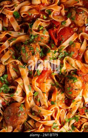 Konsistenz der Pasta in Tomatensauce mit Fleischbällchen als Hintergrund. Ein Nahschuss Pasta mit Tomatensauce. Makrofoto. Tagliatelle Pasta mit Tomaten Stockfoto