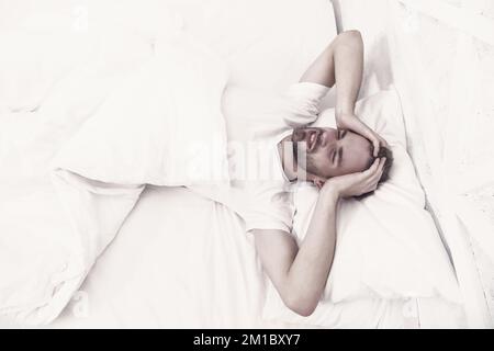 Schlafstörungen können morgens zu Kopfschmerzen führen. Ein hübscher Mann, der sich im Bett entspannt. Schnarchen kann das Risiko von Kopfschmerzen erhöhen. Gemeinsames Symptom der Schlafapnoe Stockfoto