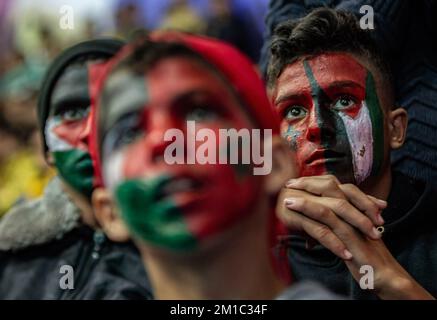 Gaza, Palästina. 10.. Dezember 2022. Junge Palästinenser mit bemalten Gesichtern der Flaggen Marokkos und Palästinas sehen aufmerksam die Live-Übertragung des Viertelfinalspiels der FIFA-Weltmeisterschaft zwischen Marokko und Portugal, das in Katar in der Saad Sayel Sports Hall in Gaza City stattfand. (Endstand Marokko 1-0 Portugal) Gutschrift: SOPA Images Limited/Alamy Live News Stockfoto