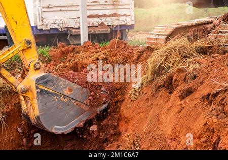 Baggerschaufel gräbt Erde zum Beladen des Lkws. Erdarbeit. Schmutzmetalleimer eines Baggerladers, der auf einer Baustelle arbeitet. Erdbewegungsmaschine. Erde Stockfoto