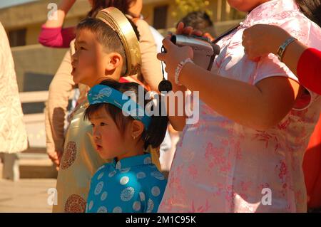 Kleine asiatische Kinder kleiden sich in traditioneller chinesischer Festkleidung und sehen sich die Feierlichkeiten zum Mondneujahr an Stockfoto