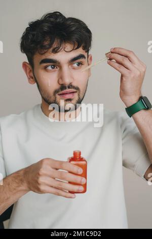 Zugeschnittenes Bild eines Mannes, der Tropfer und Flasche mit natürlichem organischem Kosmetiköl hält. Körper- und Hautpflege. Isolierter onweißer Hintergrund. Gesichtsbehandlung Stockfoto