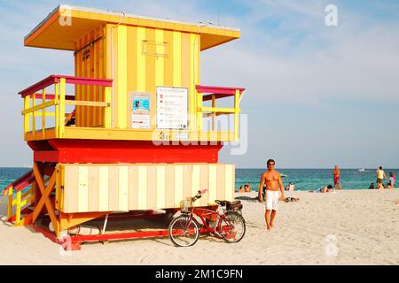 Ein junger erwachsener Strandgänger geht am farbenfrohen Art déco Third Street Lifeguard Tower in Miami Beach, Florida vorbei Stockfoto