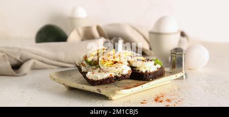 Leckere Toasts mit gekochten Eiern und Avocado auf einem weißen Tisch Stockfoto