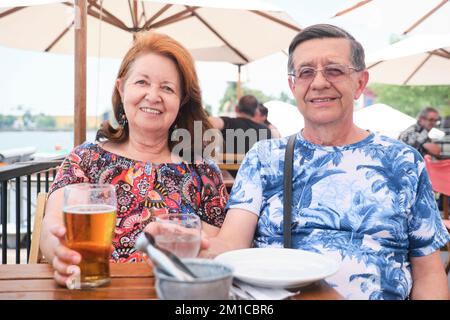 Ältere hispanische Ehepaare, die an einem Sommerabend an einem Tisch im Freien in einem Restaurant etwas kühles trinken, Bier und Wasser. Stockfoto