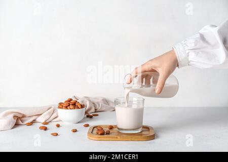 Frau, die Mandelmilch in Glas gießt, auf einem weißen Tisch Stockfoto