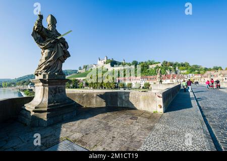 Eine Skulptur des Heiligen Kilian auf der Brücke „Alte Mainbrücke“, die den Main und das Schloss „Festung Marienberg“ auf einem Hügel in der Ferne überquert Stockfoto